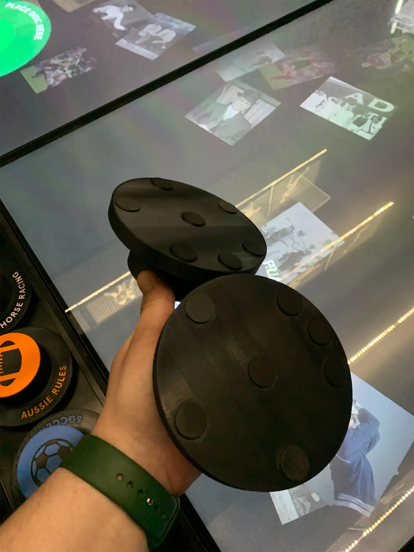 Hand holding two of the proprietary 'puck' controllers above the DISPLAX capacitive touch table during hardware testing